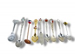 METAL PRATEADO, nove (9) pequenas colheres souvenir de coleção, confeccionadas em metais prateado, dourado e cobreado, com cabos ornamentados, torcidos e trabalhados, terminais decorados com figuras, brasões, inscrições e aplicações esmaltadas coloridas, incluindo referências turísticas como Busch Gardens, Chile, Niagara Falls, Catalina Island e outras localidades.