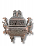 METAL ORIENTAL, um (1) incensário confeccionado em metal cobreado com decoração de dragões, pés em carrancas, alças laterais em arabescos e tampa com elementos em vazados com pega representando cães de fó, marcado no fundo, medindo 16x15x9cm.