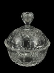 CRISTAL, uma (1) bomboniere confeccionada em cristal translúcido com lapidação de elementos geométricos e caneluras em baixo relevo com pega da tampa no feitio de flor, medindo 19x17,5cm.