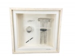 SÔNIA ROCHA, um (1) quadro decorativo com pequenas esculturas em malha de metal da artista, moldados em formato de peças de vestuário, como uma camiseta, calça, cinto e acessórios, moldura em madeira com patina branca e frente em vidro, medindo 36x38cm. Pequena borda da moldura colada.
