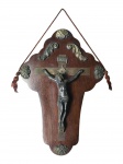 ARTE SACRA, um (1) crucifixo de parede confeccionado em estanho, decorado por elementos vegetalistas relevados e apoiados sobre placa de madeira com recortes na borda, medindo 35x24cm.