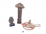 ESCULTURAS, três (3) peças artesanais em madeira, sendo: A) uma (1) coruja esculpida sobre base retangular, medindo 10,5cm de altura, B) uma (1) escultura/totem em madeira entalhada, representando figura estilizada com elemento superior em formato orgânico com sinais de cupim, medindo 21,5cm de altura e C) uma (1) peça decorativa em madeira pintada, em formato de pá/tabuleiro, com pequenas aves aplicadas com movimento ao puxar corda, medindo 19,5x11,5cm.