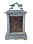 RELÓGIO, um (1) antigo de mesa, despertador, marca ANSONIA CLOCK COMPANY (fundada em Connecticut no ano de 1851, por Anson Green Phelps e mais dois relojoeiros Theodore Terry e Franklin C. Andrews, como subsidiária de sua empresa Ansônia Brass, fundada anteriormente em 1844 para fornecer laminados em latão para confecção de relógios, em 1877 adquiriram uma fábrica em New York e transferiram a maior parte de sua produção; em 1878 Thomas Edison visitou a fábrica para experimentar a combinação de relógios com o seu fonógrafo; em 1879 uma segunda fábrica foi aberta no Brooklyn; em 1880 a fábrica de New York incendiou; em 1881 foi reaberta após ter sido reconstruída no mesmo lugar; em 1883 fechou a fábrica de Connecticut; em 1929 foi vendida para Amtorg, que pertencia ao governo Soviético; em 1969 os direitos do uso do nome foram transferidos para Ansônia Clock Company, Lynnwood, Washington), modelo tipo CARRIAGE, caixa em metal prateado com sinais de oxidação, cinzelado por elementos vegetalistas, mostrador com marcas do tempo, grade frontal solta, vendido no estado, não testado e sem garantia de funcionamento, medindo 19x12x9cm.