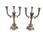 METAL PRATEADO, par (2) de candelabros para três velas confeccionados em metal espessurado a prata, hastes curvas, centro em esfera, base oval ricamente cinzelada por elementos vegetalistas, apresenta falhas na prateação, medindo 39,5x23x23cm.