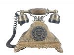 COLECIONISMO - Um (1) telefone decorativo confeccionado em resina , com base ornamentada em acabamento dourado envelhecido, relevos florais, pés trabalhados, fone duplo com detalhes em tom bronze e teclado circular com botões numéricos . Medida : 20 x 23 x 16 cm , possui bicados e quebra .