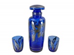 VIDROS, três (3) peças, sendo: A) 1 licoreira, medindo 24,5cm e B) 2 copos para licor, medindo 7,5x6cm, confeccionadas em vidro na tonalidade azul cobalto, decorado por elementos florais e vegetalistas filetados em prata, apresentando falhas na prateação, licoreira com bicado na borda.