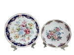 PORCELANA JSB, dois (2) pratos decorativos confeccionados em porcelana na tonalidade branca, decorado por elementos florais e vegetalistas em policromia, recortes sobre fundo azul e filetes em ouro, medindo 24cm e 20,5cm de diâmetro.