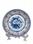PORCELANA ORIENTAL, uma (1) prato decorativo confeccionado em porcelana oriental dita: "grão de arroz" (também chamada de "rice grain porcelain" em inglês) é uma técnica tradicional chinesa e também produzida em outros países, famosa por seu delicado efeito translúcido que imita pequenos grãos de arroz incrustados na peça, elementos florais na tonalidade azul e vermelha, apresenta bicados na borda, medindo 23cm de diâmetro,