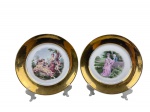 PORCELANA REAL - Par de pratos decorativos em porcelana, com ampla borda dourada e reserva central com cenas galantes  policromadas, representando personagens em trajes de época em paisagem.Medida : 23,5 cm , verso apresenta argolas coladas .