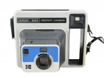 FOTOGRAFIA, uma (1) câmera instantânea antiga Kodak EK2 Instant Camera, made in U.S.A., com corpo em plástico nas cores branco, preto, azul e prata, visor lateral, lente frontal com ajuste lighten/darken, botão battery test e alça de transporte, acondicionada em caixa original com desgastes, não testada e sem garantia de funcionamento.