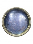 RELÓGIO, uma (1) caixa para relógio náutico confeccionado em metal com pintura marrom, aro circular em metal dourado e vidro convexo, interior com pintura preta, parte externa com sinais de oxidação, medindo 11x30cm.
