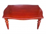 MOBILIÁRIO, uma (1) mesa de centro confeccionada em madeira, tampo recortado, saia frontal frisada e pés torneados. Peça em acabamento avermelhado, medindo 46x80x105cm.