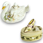 CONJUNTO DE PORTA-JOIAS EXECUTADOS EM MATERIAIS, TÉCNICAS, MODELOS, FORMATOS, TAMANHOS, UTILIDADES E PROCEDÊNCIAS DIVERSOS, COM DELICADA MODELAGEM DOS ELEMENTOS ORNAMENTAIS, COMPOSTO POR DUAS PEÇAS, SENDO: UM EM BISCUIT, REPRESENTANDO CISNE COM TAMPA REMOVÍVEL RICAMENTE ORNAMENTADO EM RELEVOS E APLICAÇÕES FLORAIS, MEDINDO 9 X 12 X 8 CM, E UM EM RESINA, EM FORMATO OVAL COM DECORAÇÃO FLORAL EM RELEVO E APLICAÇÃO DE SAPATO FEMININO SOBRE A TAMPA, MEDINDO 7 X 7 X 4 CM. APRESENTAM MARCAS DO TEMPO, USO, DESGASTES NA PATINAÇÃO E/OU PEQUENAS IMPERFEIÇÕES COMPATÍVEIS COM SUA UTILIZAÇÃO E ESTADO DE CONSERVAÇÃO, CONFORME FOTOS EXTRAS. 