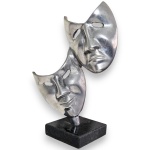 ESCULTURA EXECUTADA EM METAL COM ACABAMENTO POLIDO, REPRESENTANDO DUAS MÁSCARAS CÊNICAS ESTILIZADAS COM EXPRESSÕES CONTRASTANTES, APOIADA SOBRE BASE EM PEDRA, MEDINDO 22 X 15 X 8 CM. APRESENTA MARCAS DO TEMPO, USO, OXIDAÇÕES, PEQUENOS RISCOS E/OU IMPERFEIÇÕES COMPATÍVEIS COM SUA UTILIZAÇÃO E ESTADO DE CONSERVAÇÃO, CONFORME FOTOS EXTRAS.