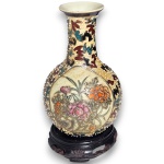 VASO EXECUTADO EM PORCELANA ESMALTADA RICAMENTE ORNAMENTADO COM DECORAÇÃO FLORAL POLICROMADA EM RESERVA CENTRAL E PADRONAGEM ORNAMENTAL CONTÍNUA NO ENTORNO, APRESENTA DETALHES EM RELEVO E PONTILHADOS EM ESMALTE, COM CORPO BOJUDO E GARGALO ALONGADO, ACOMPANHADO POR BASE EM MADEIRA ENTALHADA, DITA PEANHA, MEDINDO 15 CM. APRESENTA MARCAS DO TEMPO, USO, CRAQUELÊS NO ESMALTE, DESGASTES, PEQUENAS AVARIAS E/OU IMPERFEIÇÕES COMPATÍVEIS COM SUA UTILIZAÇÃO E ESTADO DE CONSERVAÇÃO, CONFORME FOTOS EXTRAS.