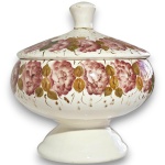 COMPOTEIRA EXECUTADA EM FAIANÇA COM PÉ, CORPO BOJUDO SUSTENTADO POR BASE PEDESTALADA CIRCULAR, APRESENTANDO DECORAÇÃO FLORAL COM GUIRLANDAS DE ROSAS E FOLHAGENS EM TODA A VOLTA, ACOMPANHADA DE TAMPA ENCIMADA COM PEGA, MEDINDO 20 X 18,5 CM. APRESENTA COLAGEM NA PEGA, MARCAS DO TEMPO, USO, PEQUENOS RISCOS, DESGASTES NO ESMALTE E/OU IMPERFEIÇÕES COMPATÍVEIS COM SUA UTILIZAÇÃO E ESTADO DE CONSERVAÇÃO, CONFORME FOTOS EXTRAS.