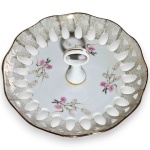 PORCELANARTE - PRATO PARA DOCES COM PEGA CENTRAL, EXECUTADO EM PORCELANA, COM BORDA ONDULADA E RECORTES VAZADOS FENESTRADOS EM TODO O CONTORNO, APRESENTANDO DECORAÇÃO FLORAL COM RAMOS E FLORES, ALÉM DE RICA ORNAMENTAÇÃO EM VIBRANTE DOURADO, POSSIVELMENTE OURO, NA BORDA E NA PEGA CENTRAL EM FORMATO DE ARGOLA, MEDINDO 8 X 19 CM. APRESENTA MARCAS DO TEMPO, USO, PEQUENOS RISCOS, DISCRETOS DESGASTES NO DOURADO PERIFÉRICO E/OU IMPERFEIÇÕES COMPATÍVEIS COM SUA UTILIZAÇÃO E ESTADO DE CONSERVAÇÃO, CONFORME FOTOS EXTRAS.