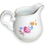 SCHMIDT - LEITEIRA, EXECUTADA EM PORCELANA ESMALTADA E VITRIFICADA, APRESENTANDO CORPO DE FORMATO BOJUDO DECORADO COM RAMOS E FLORES EM ARRANJO FLORAL NA TÉCNICA DITA DECALQUE, DOTADA DE ALÇA LATERAL ORNAMENTADA COM VOLUTAS E RELEVOS, BICO VERTEDOR VERTICALIZADO COM BORDA ONDULADA RECOADA E BASE ANELAR DE PERFIL LISO, APRESENTANDO FILETES EM DOURADO APLICADOS NAS BORDAS E NO CONTORNO DA BASE, MEDINDO 9 X 13 X 7 CM APRESENTANDO MARCAS DO TEMPO, USO, PEQUENOS RISCOS, DISCRETOS DESGASTES NO DOURADO PERIFÉRICO E/OU IMPERFEIÇÕES COMPATÍVEIS COM SUA UTILIZAÇÃO E ESTADO DE CONSERVAÇÃO, CONFORME FOTOS EXTRAS.