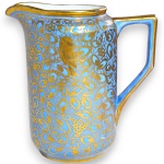 TK THUN - LEITEIRA, MADE IN CZECHOSLOVAKIA, EXECUTADA EM PORCELANA ESMALTADA E VITRIFICADA, CORPO CILÍNDRICO COM ALÇA ESTILIZADA DE LINHAS RETAS E BICO CURVO COM PONTA DITA BICO DE PATO, RICAMENTE ORNADO COM DENSA DECORAÇÃO APRESENTANDO ELEMENTOS FITOMÓRFICOS, VOLUTAS E PÁSSAROS EM INTENSO DOURADO, MEDINDO 10 X 10 X 6,5 CM. APRESENTA MARCAS DO TEMPO, USO, PEQUENOS RISCOS, DESGASTES NA DOURAÇÃO, MANCHAS, PEQUENAS AVARIAS E/OU IMPERFEIÇÕES COMPATÍVEIS COM SUA UTILIZAÇÃO E ESTADO DE CONSERVAÇÃO, CONFORME FOTOS EXTRAS.