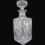 GARRAFA PARA BEBIDAS EXECUTADA EM DEMI-CRISTAL, DE FORMATO PARALELEPÍPEDO DE FACES QUADRADAS, RICAMENTE ORNADA COM LAPIDAÇÃO EM ESTRELAS MULTIFACETADAS, MALHA DE DIAMANTE E FRISOS RADIAIS EM RELEVO, DOTADA DE GARGALO AFUNILADO COM ANEL PROEMINENTE, ACOMPANHADA TAMPA DE FORMATO CIRCULAR FACETADO ENCIMADA COM PEGA EM BOTÃO DECORADO EM CONSONÂNCIA, MEDINDO 25 X 9 X 9 CM. APRESENTA MARCAS DO TEMPO, USO, PEQUENOS RISCOS, MANCHAS, PEQUENOS DESGASTES E/OU IMPERFEIÇÕES COMPATÍVEIS COM SUA UTILIZAÇÃO E ESTADO DE CONSERVAÇÃO, CONFORME FOTOS EXTRAS.