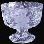 BOHEMIA - PETISQUEIRA SOBRE PEDESTAL EXECUTADA EM GROSSO CRISTAL TRANSLÚCIDO MOLDADO E LAPIDADO, COM CORPO DECORADO POR GRANDES FOLHAS DE PARREIRA SATINADAS INTERCALADAS POR CACHOS DE UVA EM RELEVO E VOLUTAS NA BORDA SUPERIOR ONDULADA, ASSENTADA SOBRE HASTE FACETADA COM BASE CANELADA DE FORMATO POLIGONAL, MEDINDO 10 X 11,5 CM. APRESENTA MARCAS DO TEMPO, USO, DESGASTES E/OU IMPERFEIÇÕES COMPATÍVEIS COM SUA UTILIZAÇÃO E ESTADO DE CONSERVAÇÃO, CONFORME FOTOS EXTRAS. ESCLAREÇA TODAS AS DÚVIDAS ANTES DE EFETUAR SEU LANCE, QUE SERÁ CONSIDERADO IRREVOGÁVEL E IRRETRATÁVEL. CONSULTE PREVIAMENTE OS TERMOS E CONDIÇÕES DISPONÍVEIS NO SITE. CONTATO (21) 98264-3000.