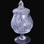 COMPOTIÈRE SOBRE PEDESTAL EXECUTADO EM DEMI-CRISTAL MOLDADO E LAPIDADO, COM CORPO BOJUDO TOTALMENTE DECORADO POR PADRÕES GEOMÉTRICOS, LAPIDAÇÕES FACETADAS, RENDILHADOS, ESTRELAS E RETÍCULOS EM RELEVO, ASSENTADO SOBRE HASTE CILÍNDRICA COM BASE CIRCULAR LISA, ACOMPANHADO DE TAMPA ENCIMADA POR PEGA EM FORMATO OGIVAL FACETADO, MEDINDO 19 X 9,5 CM. APRESENTA MARCAS DO TEMPO, USO, DESGASTES E/OU IMPERFEIÇÕES COMPATÍVEIS COM SUA UTILIZAÇÃO E ESTADO DE CONSERVAÇÃO, CONFORME FOTOS EXTRAS. ESCLAREÇA TODAS AS DÚVIDAS ANTES DE EFETUAR SEU LANCE, QUE SERÁ CONSIDERADO IRREVOGÁVEL E IRRETRATÁVEL. CONSULTE PREVIAMENTE OS TERMOS E CONDIÇÕES DISPONÍVEIS NO SITE. CONTATO (21) 98264-3000.