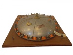 ROULETTE / JOGO DE MESA ANTIGO, POSSIVELMENTE EUROPEU, COM TABULEIRO EM MADEIRA E CÚPULA CENTRAL GIRATÓRIA EM METAL TEXTURIZADO PRATEADO, DECORADA COM CENAS EQUESTRES E FIGURAS , ARO EXTERNO COM NUMERAÇÃO EM TONS DE PRETO E LARANJA, EM ESTILO CLÁSSICO DE CASSINO, APRESENTANDO MECANISMO MANUAL COM ALAVANCA LATERAL. REMETENDO AOS ANTIGOS JOGOS DE SALÃO E ENTRETENIMENTO DA PRIMEIRA METADE DO SÉCULO XX. MEDIDAS:  15 x 45 x 45 cmAPRESENTA DESGASTES, MARCAS DO TEMPO E SINAIS DE USO COMPATÍVEIS COM SUA ANTIGUIDADE, O QUE LHE CONFERE AUTENTICIDADE E CHARME HISTÓRICO.