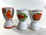 TRÊS PORTA OVOS EM PORCELANA NACIONAL COM POLICROMIA. MEDIDAS: 9 CM / 9 CM / 9,5 CM