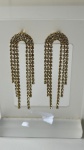 SEMI JÓIAS - Brinco folheado a ouro com design moderno em arco e franjas de strass pendentes. Peça leve, com movimento e brilho intenso, ideal para festas e produções elegantes.