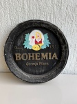 OBJETOS DECORATIVOS - Placa decorativa em gesso com tema Bohemia Cerveja Pilsen, na cor preta, com detalhes em alto relevo e imagem central colorida. Mede aproximadamente 40cm de diâmetro. Peça com marcas de uso, desgaste na pintura, pequenos pontos descascados e sinais do tempo.