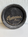 OBJETOS DECORATIVOS - Placa decorativa em gesso com tema Budweiser Budvar, na cor preta, com detalhes em alto relevo e pintura em tom dourado. Mede aproximadamente 40cm de diâmetro. Peça com marcas de uso, desgaste na pintura, pontos descascados e sinais do tempo.