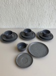 PORCELANA - Conjunto de café cinza com acabamento mesclado, contendo 4 xícaras, 4 pires de aproximadamente 15cm de diâmetro e 4 pratos de aproximadamente 20,5cm de diâmetro. Peças em bom estado geral, com design moderno e acabamento fosco/texturizado.