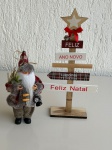 OBJETOS DECORATIVOS - Lote com 2 itens natalinos - [Item 1] Papai Noel decorativo em tecido, com roupa vermelha e cinza, lanterna e saco de gravetos, medindo aproximadamente 20cm de altura; [Item 2] Árvore decorativa de madeira com estrela no topo e placas com dizeres `Feliz Natal` e `Ano Novo`, medindo aproximadamente 36x18cm. Peças em bom estado geral, com sinais leves de uso.