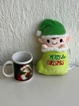 OBJETOS DECORATIVOS - Lote com 2 itens natalinos - [Item 1] Caneca de cerâmica branca com estampa de Papai Noel; [Item 2] Pelúcia natalina Merry Christmas em formato de elfo dentro de saco verde, medindo aproximadamente 23x14x8cm. Peças em bom estado geral.