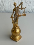 OBJETOS DECORATIVOS - Estátua decorativa da Justiça em resina na cor dourada, segurando espada e balança com correntes. Mede aproximadamente 23,5cm de altura por 7cm de diâmetro na base. Peça com detalhes ornamentais e acabamento com brilho, em bom estado geral.