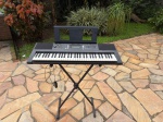 INSTRUMENTOS MUSICAIS - Teclado Yamaha PSR-E343, na cor preta, acompanhado de suporte em X, fonte de alimentação e suporte para partitura. Item com teclas, visor digital, alto-falantes embutidos e diversos botões de configuração. Funcionando e em excelente estado de conservação.