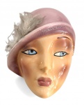 Máscara para parede em cerâmica europeia esmaltada representando rosto feminino estilizado, com pintura policromada, chapéu em tom rosado e aplicação de pena. Peça de caráter decorativo, com estética vintage. Mede 22 x 16 cm.