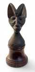 AFRICA - Antiga escultura em bronze maciço cinzelado representando figura antropomórfica de origem africana, com feições estilizadas, orelhas alongadas e expressão marcante. Corpo torneado em base cilíndrica, com furo inferior sugerindo possível uso como elemento de encaixe (tampa, bastão ou peça ritualística. apoiada sobre base de madeira. Mede 27 cm de altura.