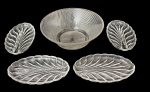 Conjunto em vidro prensado incolor composto por centro de mesa circular canelado e quatro travessas em formato de folha, com elegante desenho em relevo. Peças decorativas de apelo clássico. Medida do maior 23 cm diâmetro.