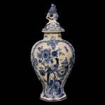DELFT - Potiche em faiança holandesa, de formato balaústre decorado em azul sobre branco. Bojo abaulado, ornado por pássaros e ramos floridos em reservas. Gargalo retraído, encimado por tampa cônica de mesmo estilo com borda saliente. Apresenta pega moldada com arabescos entrelaçados. Marca do artista sob a base. 41 x 20 x 13 cm.