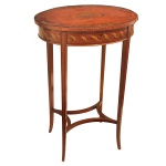 Mesa de costura (ou "work table") de estilo clássico inglês. Tampo oval com dobradiça que revela um compartimento interno forrado e dividido para materiais de costura. Decoração lateral com faixas de marchetaria ou filetes contrastantes. Pernas finas e cônicas unidas por uma travessa em formato de "X" com um medalhão central. 75 x 52 x 39 cm.