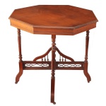 Séc. XIX - Mesa lateral oitavada em madeira nobre,  do estilo vitoriano, Tampo de formato oitavado com bordas moldadas sustentado por pernas finas torneadas que se conectam a uma travessa em formato de cruz. Abaixo do tampo, a estrutura apresenta grades e arcos decorativos vazados recortados (fretwork), típicos do movimento britânico Arts & Crafts. 72 x 77 x 77 cm.