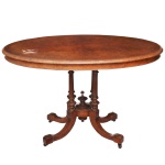 Séc. XIX - Mesa de apresentação vitoriana em madeira nobre também conhecida como loo table. Feita em madeira de nogueira com tampo folheado em rádica de alta qualidade. Apresenta formato oval com bordas molduradas e acabamento refinado. O tampo é sustentado por uma coluna central composta por quatro colunas torneadas em anel, unidas no centro por um refinado pináculo em formato de urna. A base se divide em quatro pernas recurvas de estilo cabriole com entalhes decorativos, terminando em pés de voluta equipados com seus rodízios originais. Tampo necessitando de pequeno restauro (manchada). 75 x 113 x 80 cm.