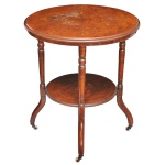 Séc. XIX - Mesa lateral clássica, inspirada no requintado estilo inglês. Apresenta um tampo superior redondo e um platô inferior idêntico, conectados por quatro colunas centrais com torneamento clássico.  : em madeira nobre com um rico trabalho de marchetaria floral e geométrica central, cercada por detalhes circulares incrustados. Os pés curvados contam com pequenas rodinhas metálicas (rodízios) de estilo antigo.b65 x 58 cm.