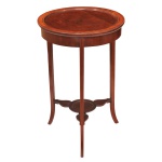 Mesa lateral de estilo Eduardiano, datada do séc. XX. Construída em madeira nobre, predominantemente mogno (mahogany), exibindo tons quentes e ricos.: Apresenta formato redondo, pernas longas e finas que se abrem levemente para fora em direção à base, conferindo leveza e sofisticação à peça. Destaca-se pelo fino trabalho de marchetaria com filetes de madeira contrastante em satinwood) nas bordas e nas pernas. No centro, as pernas são unidas por uma prateleira inferior decorativo em formato de trevo. 68 x 44 cm.