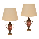 Par de elegantes luminárias de mesa  em cristal da Boêmia montado em uma base ornamental, ornados em overlay de cor rubi.  Apresentam lapidação ornamentada por raiados e ramos de trigo sobre fundos em treliças. Bases afuniladas apoiadas em anelados. Montagens em bronze dourado com alças laterais em S e peanhas quadrangulares recortadas. Gargalos em corneta, encimados por cúpula de modelo cônico tradicional em tecido de cor bege. 70 cm (MT) 30 x 44 cm (cúpula).