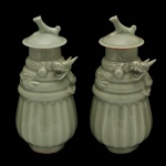 Par de vasos em porcelana chinesa, revestidos por cobertas celadon de cor verde água. Bojos cônicos moldados por gomos, encimados por anelados com dragões aplicados em relevo à volta. Gargalos reto com tampas abauladas e pegas no formato de Cães de Fó. Bases retraídas circulares. 26 x 12 cm.