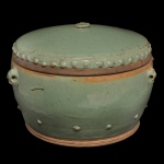 CHINA. Final séc. XVII / Séc XVIII - Pote circular em porcelana chinesa, revestido por coberta celadon de cor verde água. Bojo abaulado, ladeado por argolas e ornado por discretas bolotas na parte inferior. Tampa levemente abobadada, bordada por tachas e encimada por pega circular. Base com duplo anelado. 20 x 32 cm.
