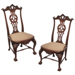 Par de cadeiras antigas no estilo inglês Chippendale, famoso por sua elegância clássica e riqueza de detalhes entalhados à mão. Feitas em madeira de lei maciça, tradicionalmente em mogno ou jacarandá. Apresenta um trabalhado vazado rebuscado com padrões recortados e silhueta sinuosa característica do período georgiano. As pernas dianteiras são no estilo cabriolet (curvas), terminando no icônico detalhe entalhado de garra de águia segurando uma bola. Estofamento removível revestido com tecido listrado clássico em tons neutros.  106 x 55 x 44 cm.