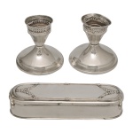 Conjunto de 2 lotes em metal espessurado a prata, sendo: A) Par  de castiçais baixos de formato circular. Possui uma borda superior vazada em estilo grade (pierced rim) e detalhes canelados discretos ao redor de sua base circular. Marca no fundo  Sterling Weighted. Bases superiores com amassados. B) Caixa para toucador em metal espessurado a prata. Apresenta cantos arredondados e linhas clássicas molduradas. A tampa plana traz detalhes decorativos em relevo nas extremidades, com ramos, folhas e guirlandas florais estilizadas